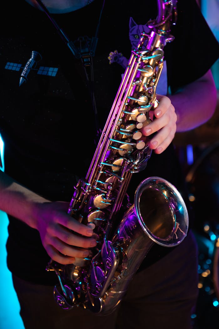 Vibrant close-up of hands playing a saxophone under colorful stage lighting.